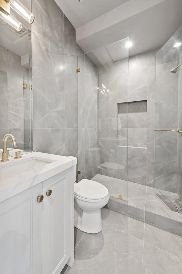 bathroom featuring tiled shower, vanity, toilet, and tile walls