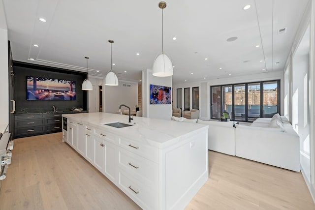 kitchen featuring white cabinetry, sink, light stone countertops, a large island with sink, and decorative light fixtures