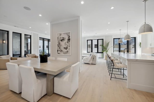 dining area featuring ornamental molding, sink, a wealth of natural light, and light hardwood / wood-style flooring