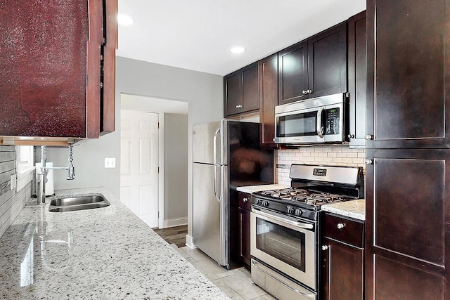 kitchen with tasteful backsplash, a sink, appliances with stainless steel finishes, light stone countertops, and recessed lighting