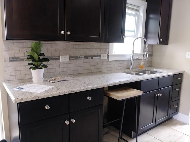 kitchen with light tile patterned flooring, a sink, light stone counters, and tasteful backsplash