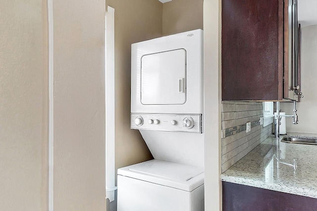 clothes washing area featuring laundry area, stacked washer / dryer, and a sink