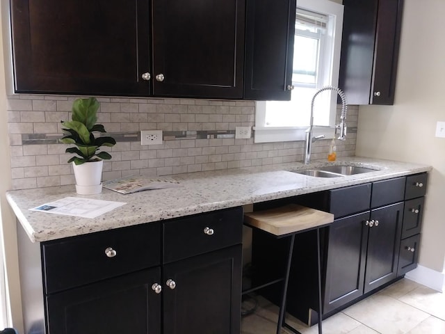 kitchen featuring light stone counters, sink, light tile patterned floors, and tasteful backsplash