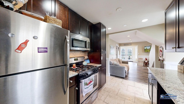 kitchen featuring french doors, dark brown cabinets, appliances with stainless steel finishes, light stone countertops, and decorative backsplash