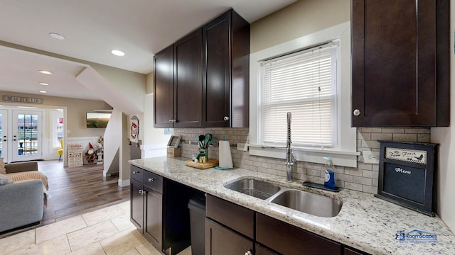 kitchen with sink, backsplash, dark brown cabinets, light stone counters, and french doors