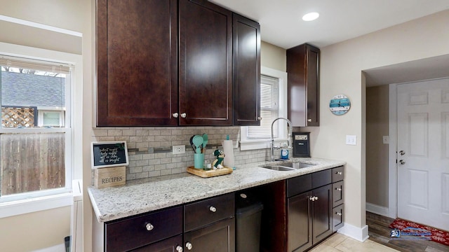 kitchen with tasteful backsplash, sink, light stone countertops, and dark brown cabinetry