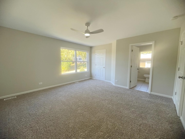 unfurnished bedroom with light colored carpet, ensuite bath, multiple windows, and ceiling fan