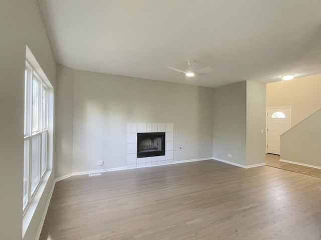 unfurnished living room featuring ceiling fan, a tiled fireplace, and light hardwood / wood-style flooring