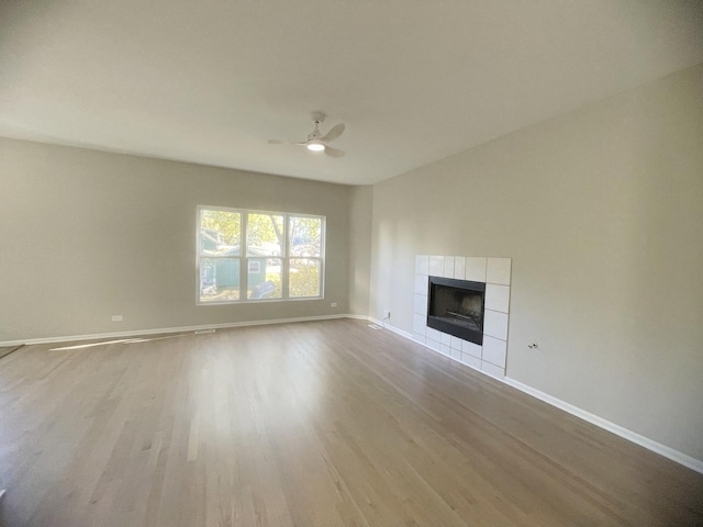 unfurnished living room featuring a tile fireplace, light hardwood / wood-style flooring, and ceiling fan