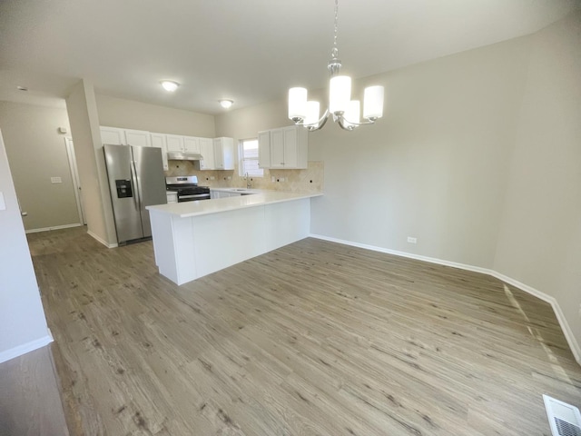 kitchen featuring kitchen peninsula, appliances with stainless steel finishes, decorative light fixtures, light hardwood / wood-style floors, and white cabinetry