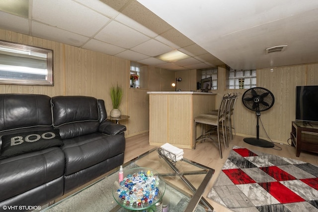 living room with light wood-type flooring, a paneled ceiling, and wood walls