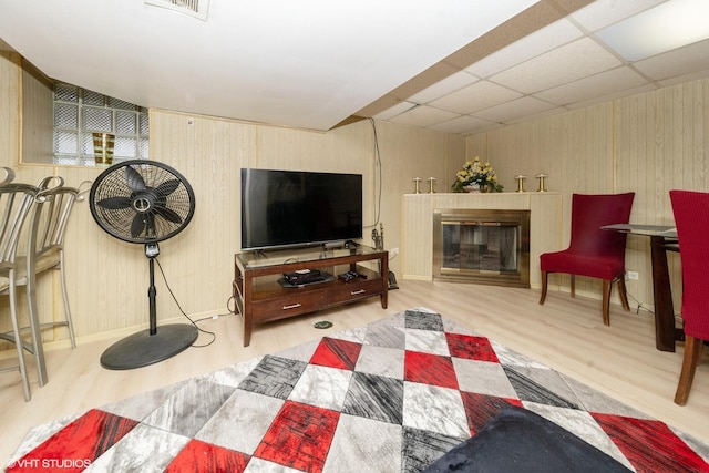 living room featuring light hardwood / wood-style flooring, a drop ceiling, and wood walls