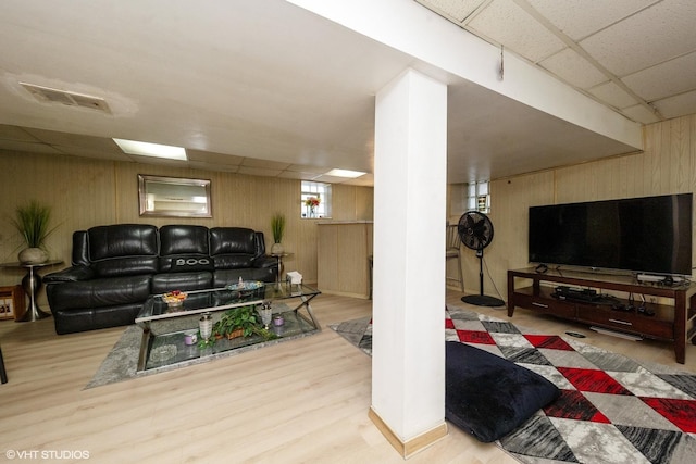 living room with light hardwood / wood-style flooring, a drop ceiling, and wood walls