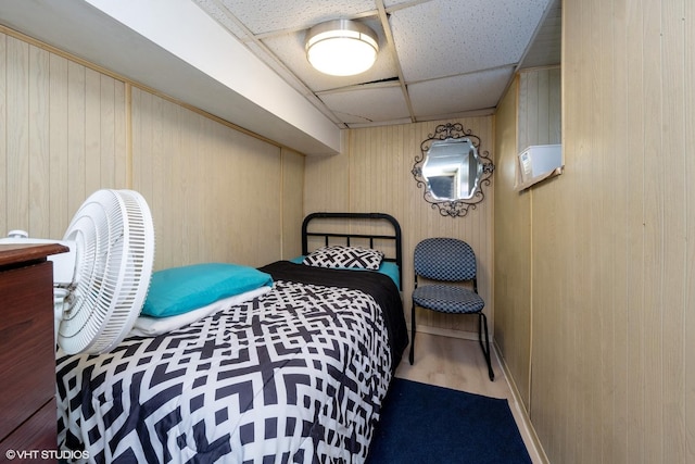 bedroom with a paneled ceiling, wood-type flooring, and wooden walls