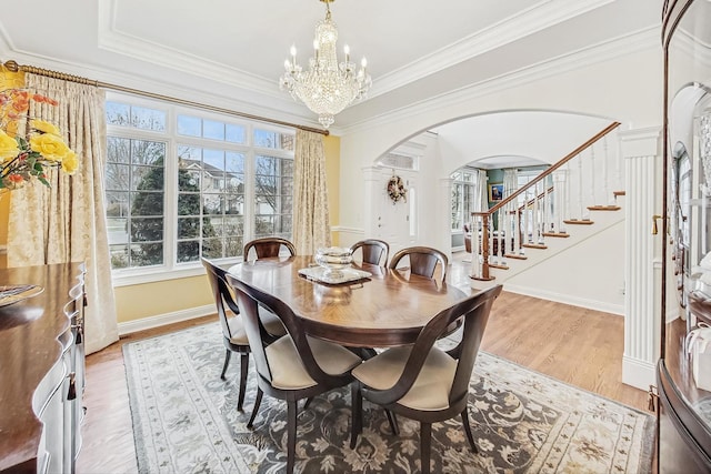 dining area with arched walkways, stairs, crown molding, light wood-style floors, and a notable chandelier