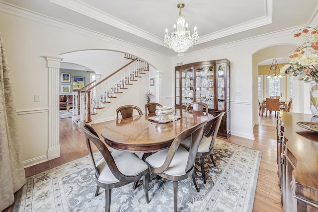 dining room featuring arched walkways, crown molding, light wood finished floors, a chandelier, and stairs