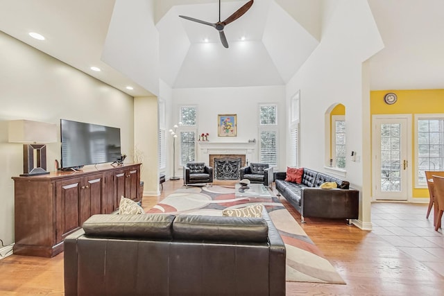 living room featuring ceiling fan, light wood-type flooring, a fireplace, and a towering ceiling