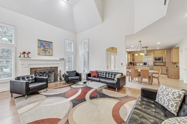 living area featuring a chandelier, recessed lighting, a premium fireplace, a towering ceiling, and light wood-style floors