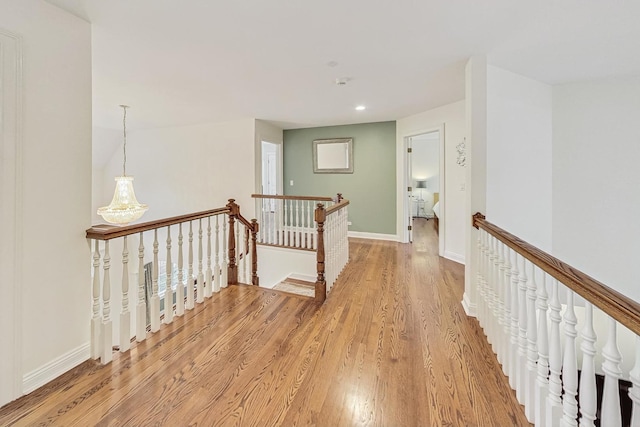 hall featuring light wood-style floors, baseboards, and an upstairs landing