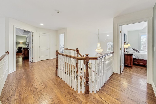 hall with baseboards, an upstairs landing, and light wood-style floors