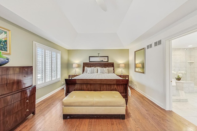 bedroom with a tray ceiling, visible vents, baseboards, and wood finished floors