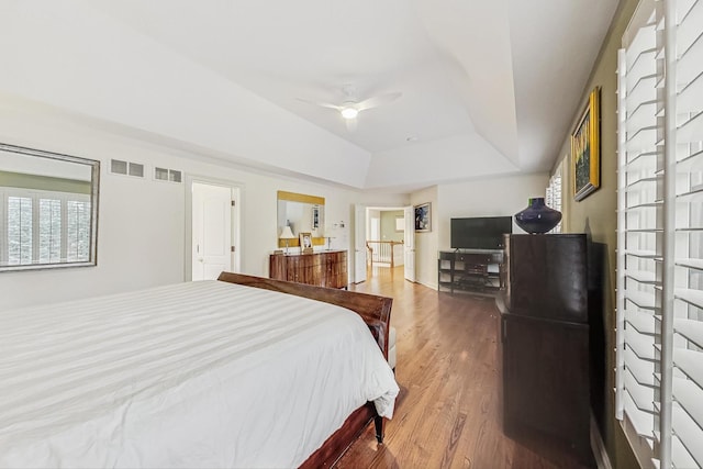 bedroom with a tray ceiling, wood finished floors, and visible vents