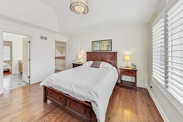 bedroom with ensuite bath, baseboards, visible vents, and wood finished floors