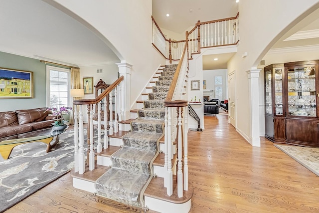 staircase featuring crown molding, arched walkways, decorative columns, and wood finished floors