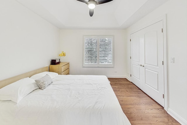 bedroom with ceiling fan, baseboards, a raised ceiling, and wood finished floors