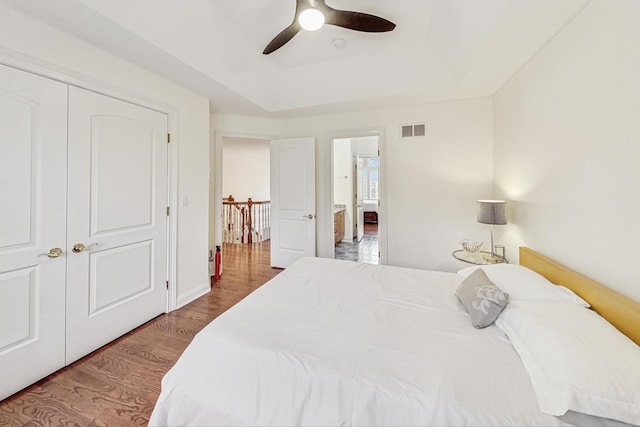 bedroom with a ceiling fan, visible vents, a raised ceiling, and wood finished floors