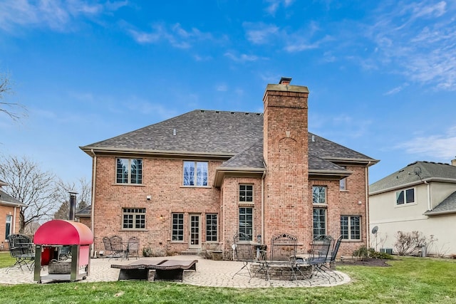 rear view of property with brick siding, roof with shingles, a fire pit, and a patio