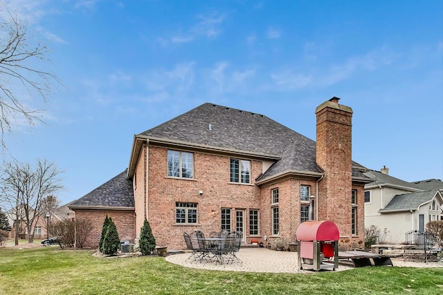 back of property with a yard, roof with shingles, a patio, and brick siding