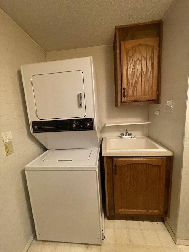 washroom featuring stacked washer / dryer, sink, cabinets, and a textured ceiling