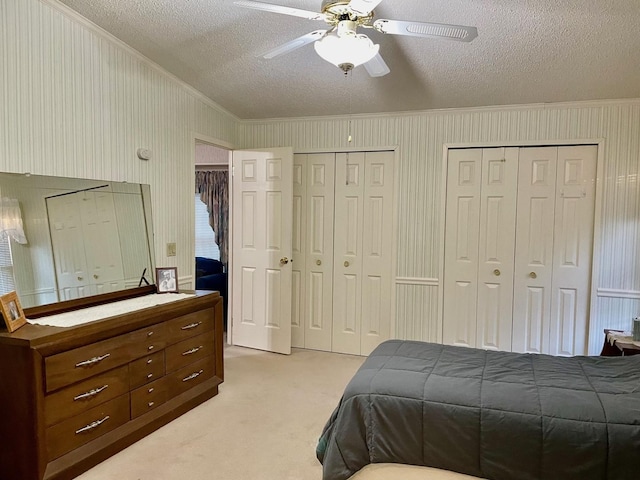 carpeted bedroom featuring ceiling fan, ornamental molding, a textured ceiling, and multiple closets