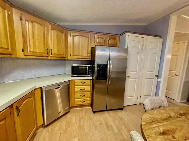 kitchen with light hardwood / wood-style floors, ornamental molding, appliances with stainless steel finishes, and vaulted ceiling