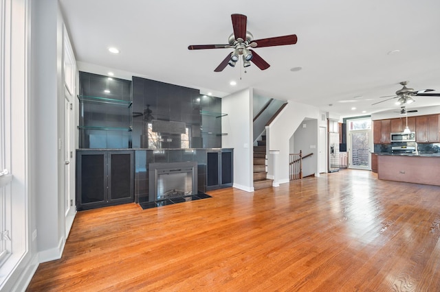 unfurnished living room with a tile fireplace, light wood-type flooring, and ceiling fan