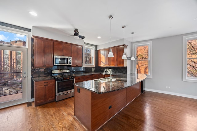 kitchen with sink, hanging light fixtures, decorative backsplash, kitchen peninsula, and stainless steel appliances