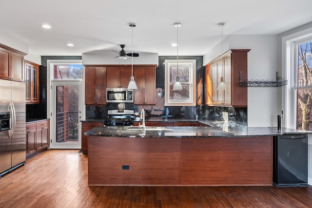 kitchen featuring pendant lighting, backsplash, hardwood / wood-style flooring, appliances with stainless steel finishes, and kitchen peninsula