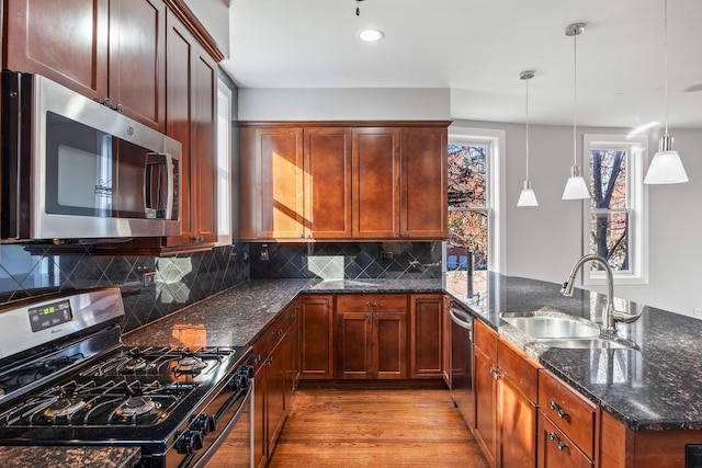 kitchen with dark stone counters, hanging light fixtures, sink, appliances with stainless steel finishes, and light hardwood / wood-style floors