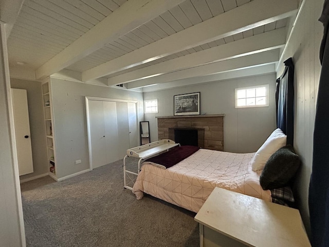 bedroom with carpet flooring, beam ceiling, and a stone fireplace