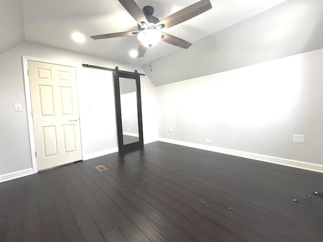 unfurnished bedroom with dark hardwood / wood-style flooring, a barn door, ceiling fan, and lofted ceiling