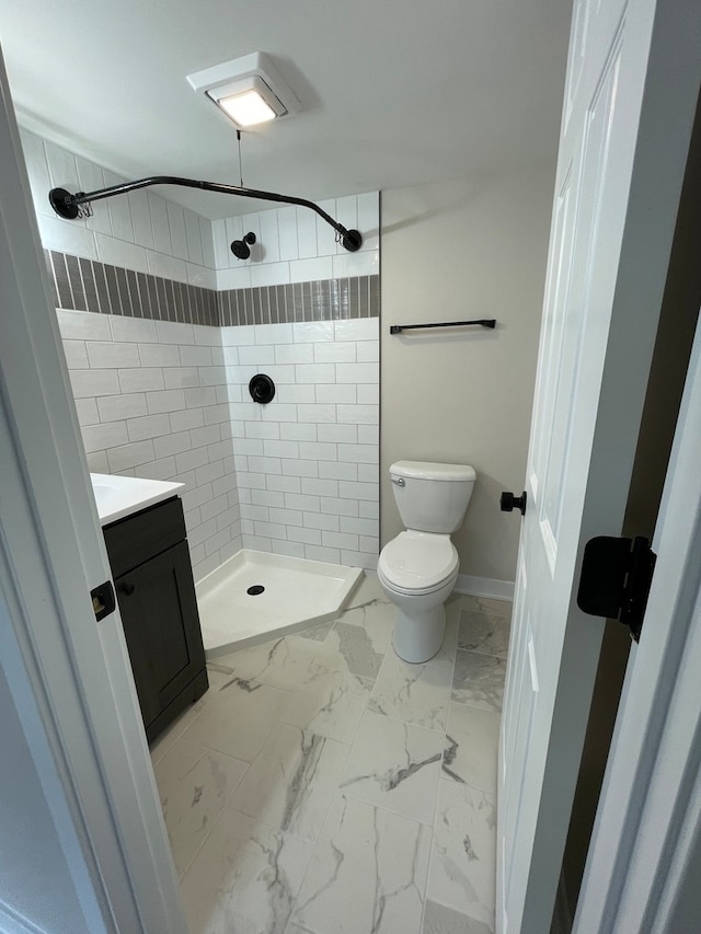 bathroom with a tile shower, vanity, and toilet