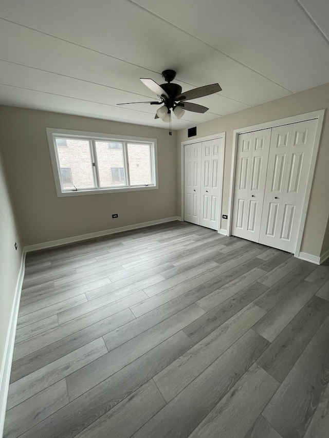 unfurnished bedroom featuring ceiling fan, two closets, and light wood-type flooring