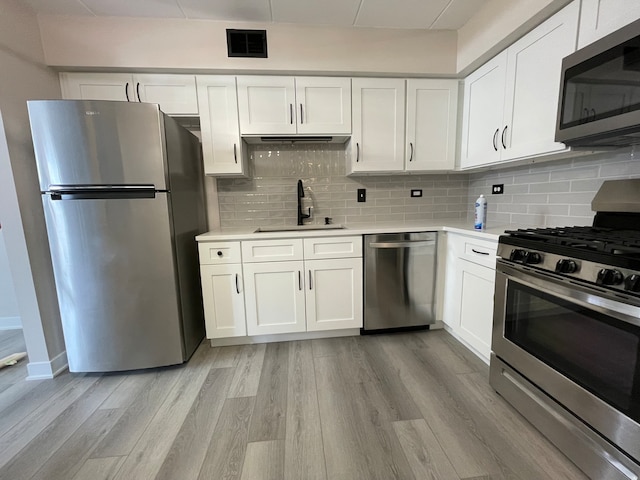 kitchen with appliances with stainless steel finishes, backsplash, sink, light hardwood / wood-style floors, and white cabinetry