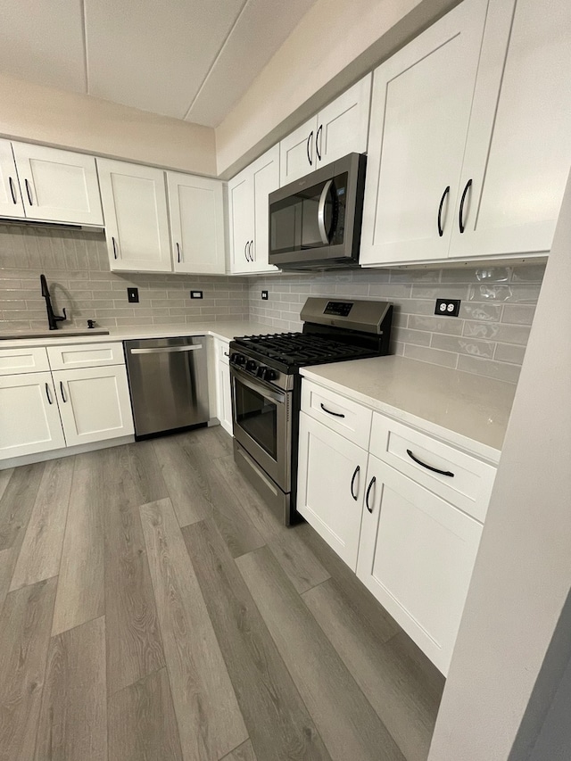 kitchen with white cabinets, light hardwood / wood-style floors, stainless steel appliances, and tasteful backsplash