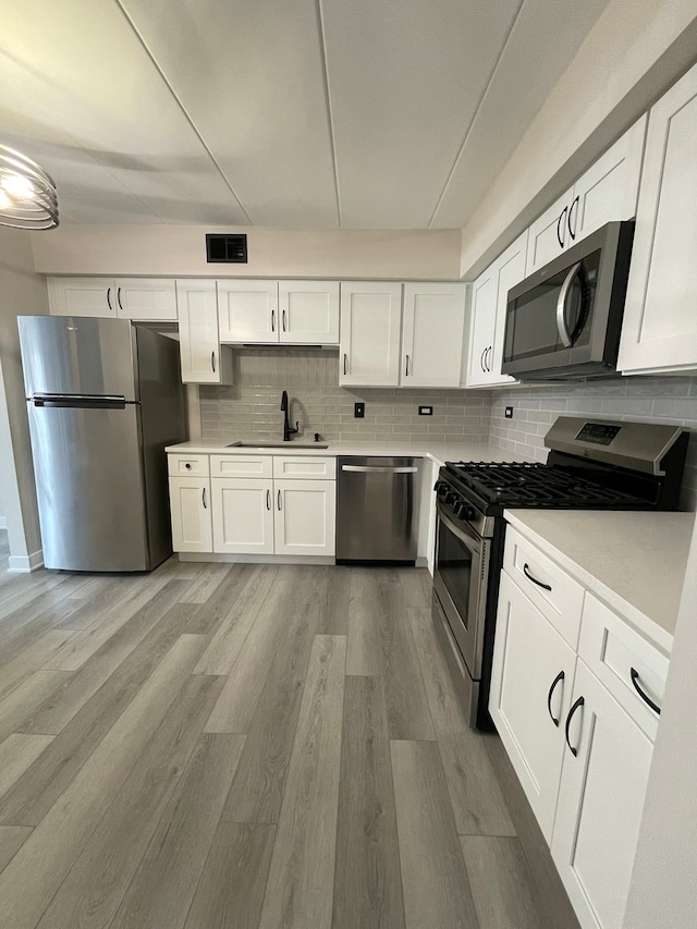 kitchen with backsplash, white cabinets, sink, light wood-type flooring, and appliances with stainless steel finishes