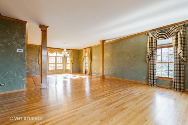 empty room featuring decorative columns, crown molding, a wealth of natural light, and light hardwood / wood-style flooring