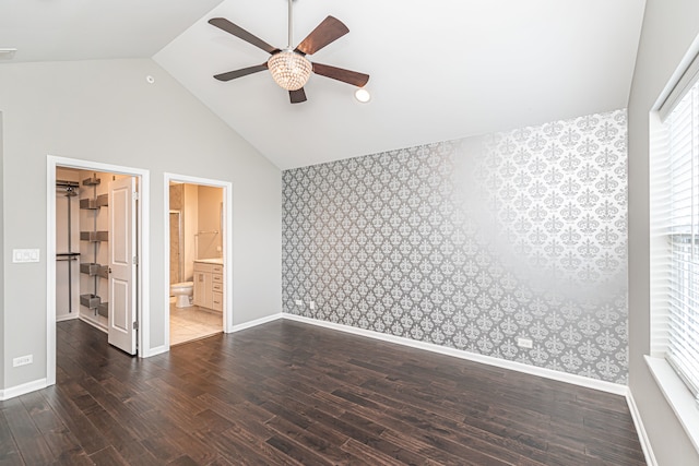 unfurnished bedroom featuring a walk in closet, ensuite bath, ceiling fan, dark wood-type flooring, and high vaulted ceiling