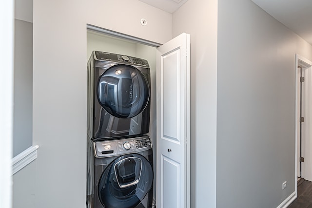 laundry area with stacked washer / drying machine and dark hardwood / wood-style flooring