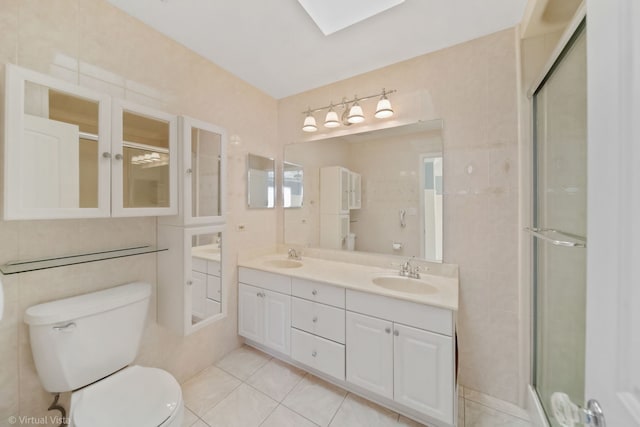 bathroom with a skylight, a stall shower, tile walls, toilet, and a sink